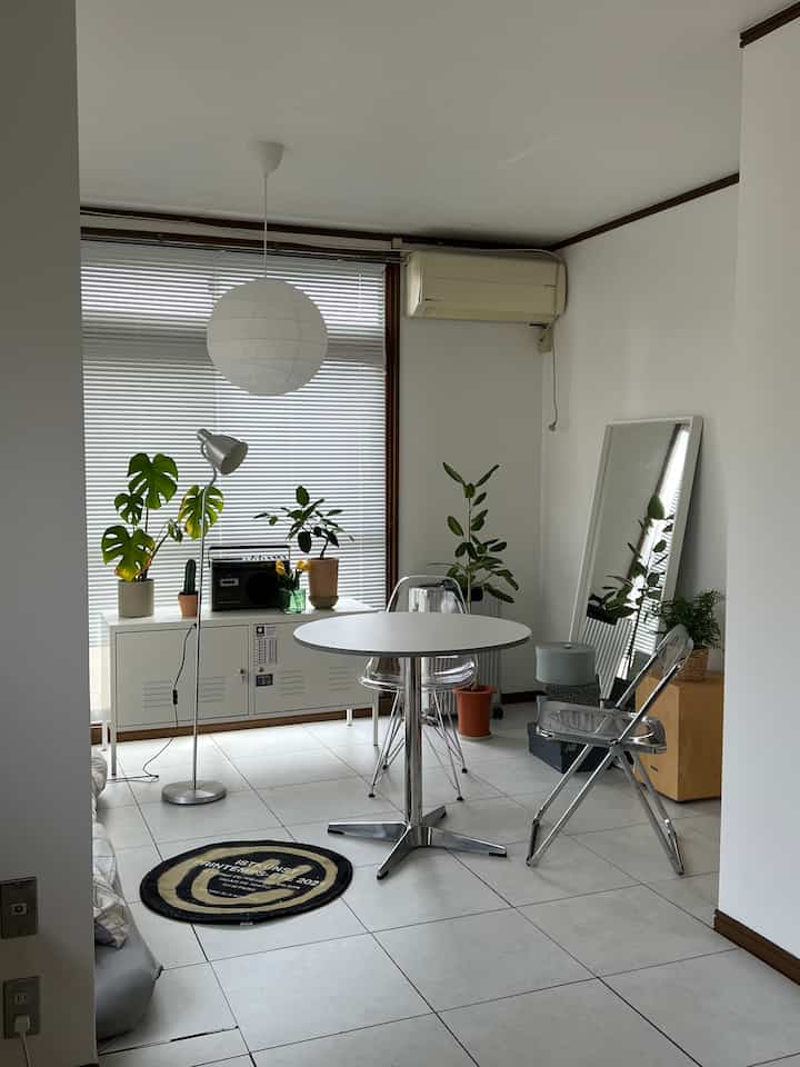 ホワイトとシルバーのトーンのリビング、丸いダイニングテーブルと透明なダイニングチェア、フロアランプと植物が配置されたシンプルでモダンな印象的な空間