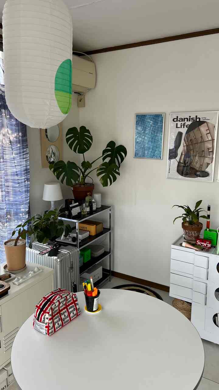 白とナチュラルカラーの調和がとれたコンパクトなリビングルーム、丸いダイニングテーブルと複数の植物が配置されたシンプルで落ち着いたインテリア