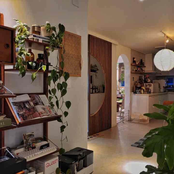 ナチュラルなブラウンとホワイトの色調で、丸い木製のドアが印象的なリビングとキッチン空間、多くの植物が配置された雰囲気のあるインテリア