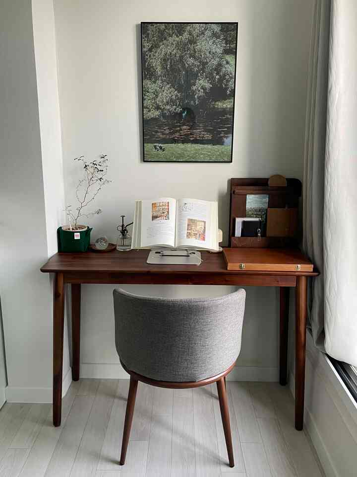 白い壁とカーテン、木目調のデスクとグレーのアームチェアが配置されたミニマルなホームオフィス
