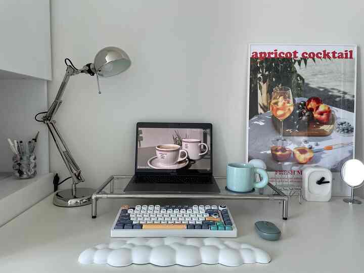 白とシルバーのシンプルなホームオフィスデスク、ノートパソコンとデスクランプ、ポスターが配置された印象的な作業空間