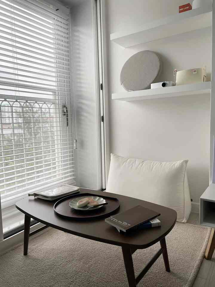 明るいナチュラルトーンの小さなリビング、多目的な木製テーブルとクリーム色のクッションが落ち着いた雰囲気を演出