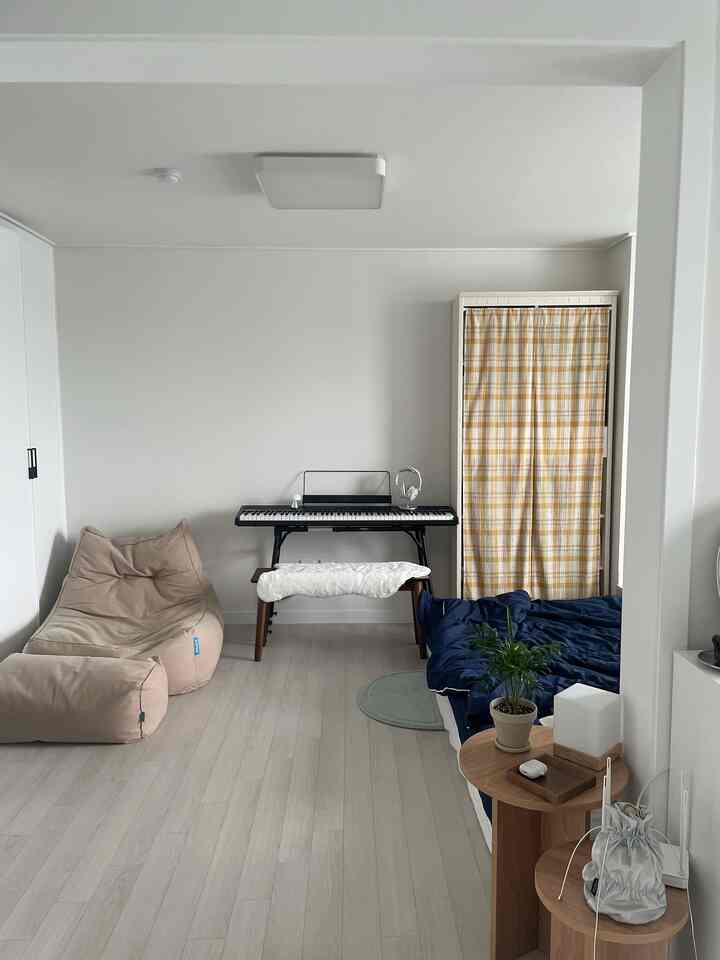 白とナチュラルウッドトーンの寝室に、ベージュのビーズクッションとデジタルピアノが配置されたシンプルで居心地の良いインテリア