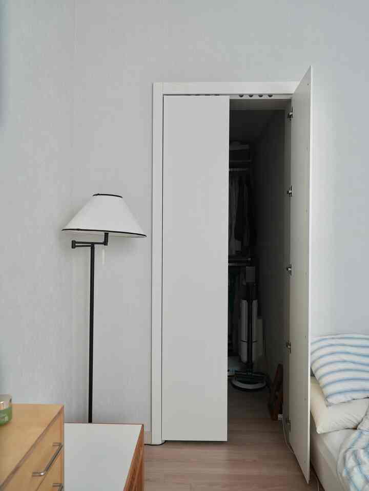 ホワイトとナチュラルカラーの寝室、フロアランプと開いたウォークインクローゼットが見えるシンプルな空間