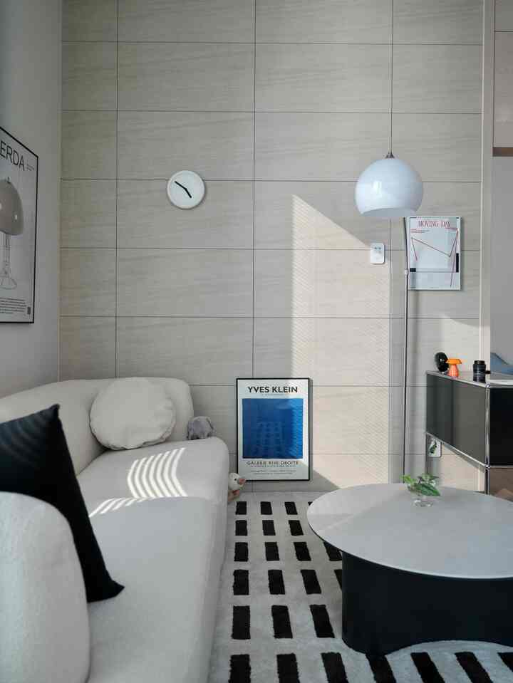 白とグレーのトーンのリビング、ミッドセンチュリーモダンスタイルのソファとラグ、テーブルランプと額縁が配置された印象的なインテリア