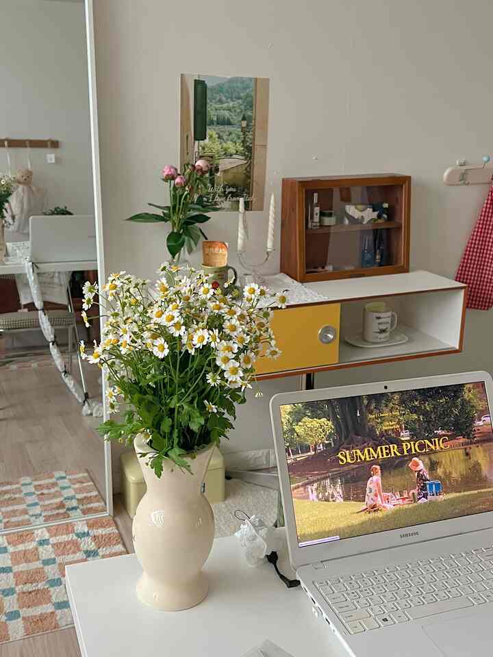 白とナチュラルカラーのリビング、ホワイトデスクと黄色の収納棚、花々が配置された雰囲気のあるインテリア