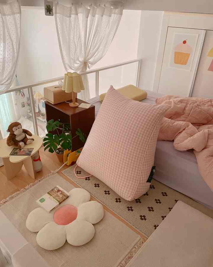 ピンクとナチュラルな色調のコンパクトな寝室で、大きなギンガムチェック柄クッションと柔らかな寝具が配置された雰囲気のあるインテリア