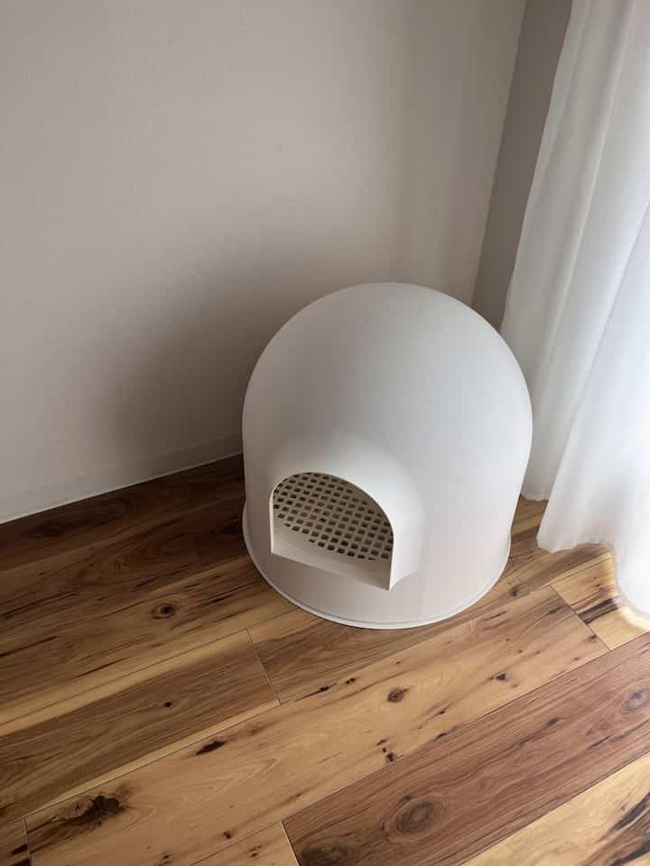 白いモダンな形状の猫トイレが木目調の床とベージュの壁のある狭い部屋の隅に配置された清潔感のあるインテリア