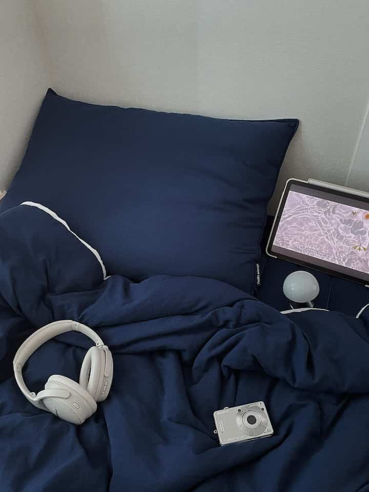 深いネイビーの寝具が配置された寝室、ヘッドフォンとデジタルカメラが置かれ、落ち着いたモダンな雰囲気を醸し出すインテリア