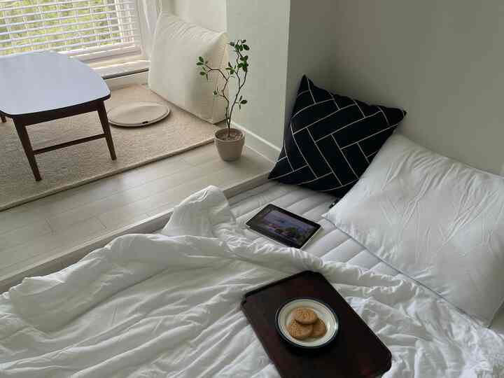 ホワイトとブラウンのトーンが特徴のワンルームリビング兼寝室、コーヒーテーブルとクッション、小さな観葉植物が配置された雰囲気のあるインテリア