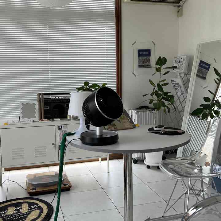 白を基調としたコンパクトな部屋、丸いテーブルとブラインド、植物が配置されたシンプルなインテリア空間