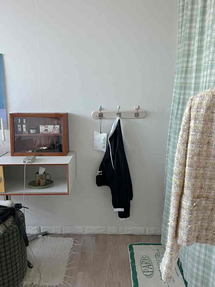 白い壁と木目調の床が特徴のミニマルな玄関スペース、壁掛け化粧台と壁のフックにかけられたジャケットが配置された空間