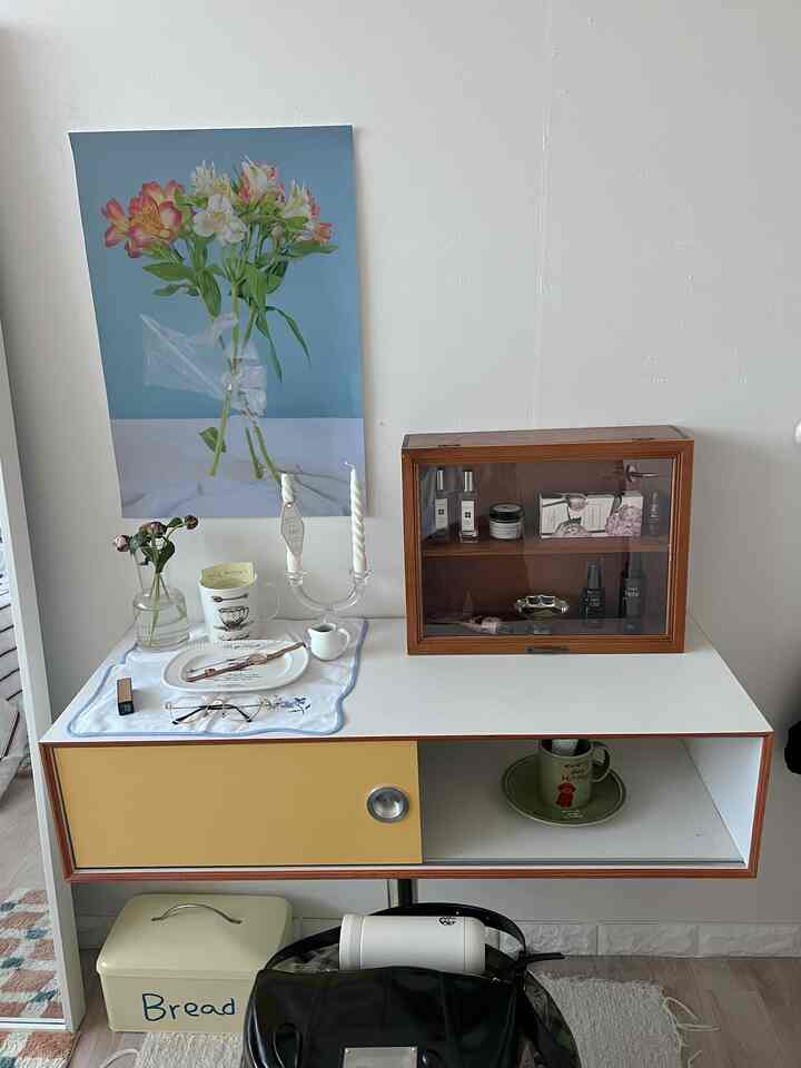 ホワイトとイエローのコンソールテーブルにポスター、キャンドル、化粧品のディスプレイボックスが配置されたミニマルな空間