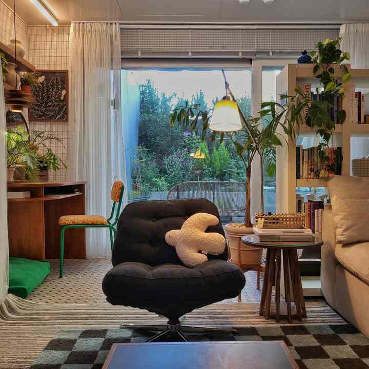 ベージュのソファと黒のアームチェアがあるナチュラルモダンなリビング、大きな窓と豊かな植物が配置された雰囲気のあるインテリア