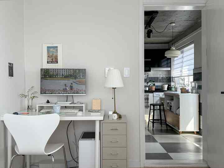白とベージュのトーンのホームオフィス空間、シンプルで自然な印象のデスクとキッチンが見える居心地の良いインテリア