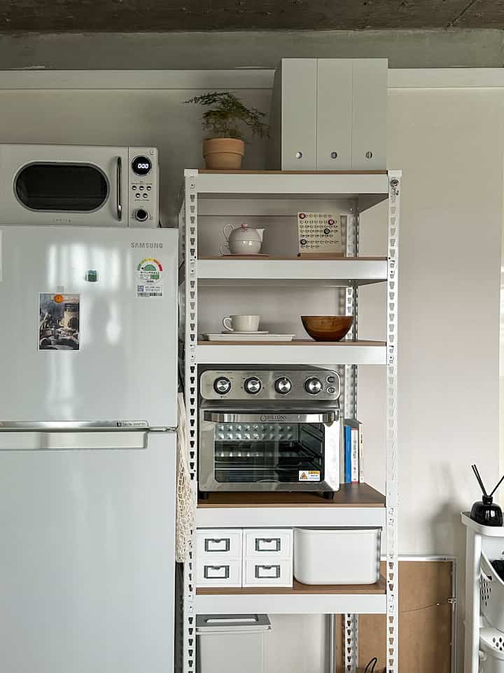 白と茶色のトーンのキッチンスペース、組み立て式棚と電子レンジが配置されたモダンで整った雰囲気のインテリア