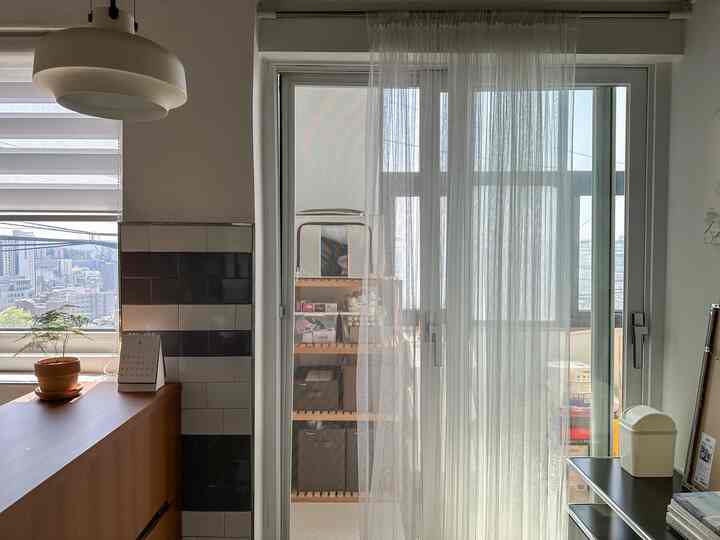 白と木目調の調和したバルコニー空間、レースカーテンと棚を使った実用的で清潔感のある収納スペース