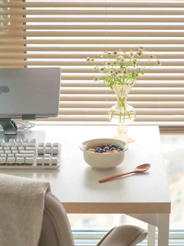 ホワイトトーンのホームオフィス、清潔感あるデスクにノートパソコンと花瓶が置かれたミニマルな作業空間