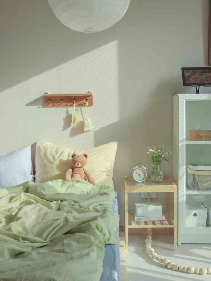 パステルベージュとライトグリーンの色調の寝室、木製ナイトテーブルとテディベア、花瓶が配された温かみのある空間