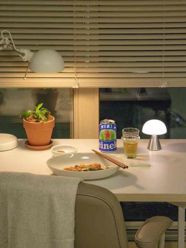 白を基調としたキッチンのデスクスペース、簡単な食事と飲み物、植物と照明が配置された落ち着いた雰囲気のインテリア