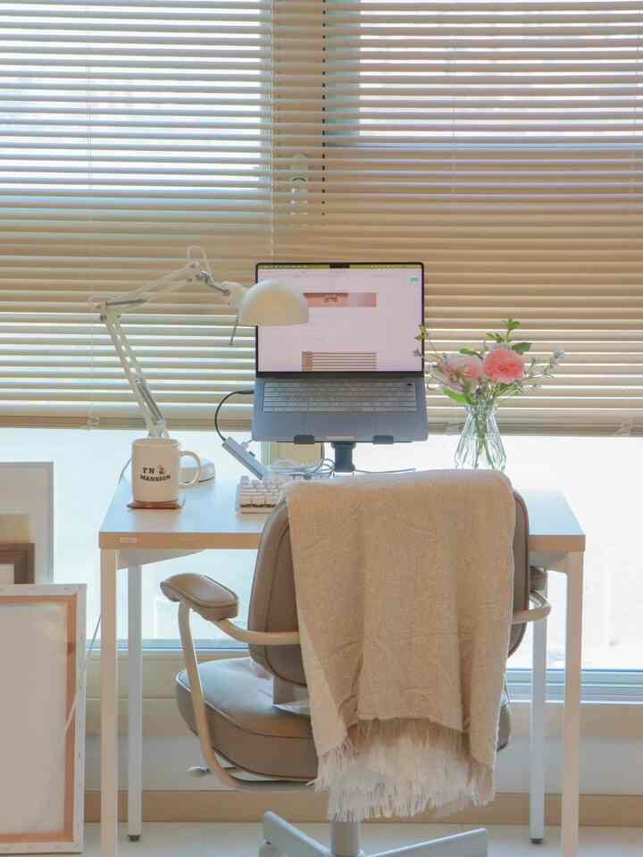 ナチュラルなベージュとホワイト調のワンルームホームオフィス、窓際にデスクとオフィスチェアが配置された雰囲気のあるインテリア