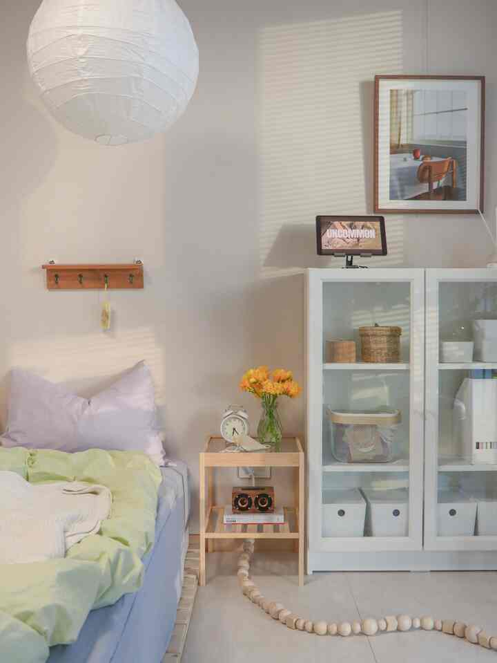 明るい白と木目調の寝室、ベッドとナイトテーブル、書棚が配置された落ち着いた印象的な空間