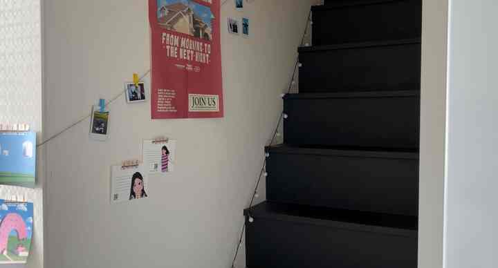 白い壁と黒い階段、ポスターと写真ガーランド、ストリングライトが配された雰囲気のあるロフトの階段空間