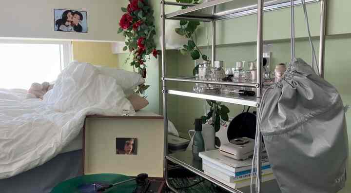 淡い緑色と白を基調とした寝室、白い寝具とBluetoothターンテーブル、香水が配置されたシンプルで居心地の良い空間