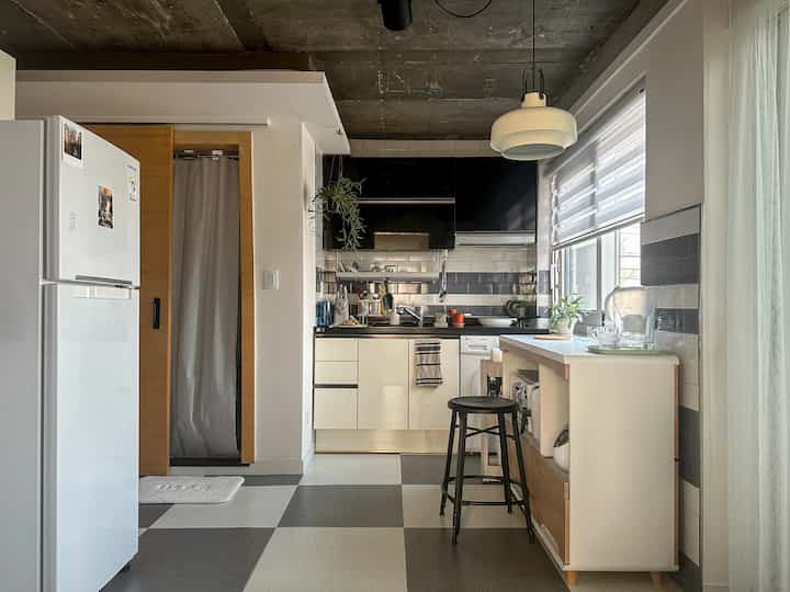 白と黒の色調のキッチン、ブラインドとスツールが配置されたモダンでナチュラルなワンルームのインテリア