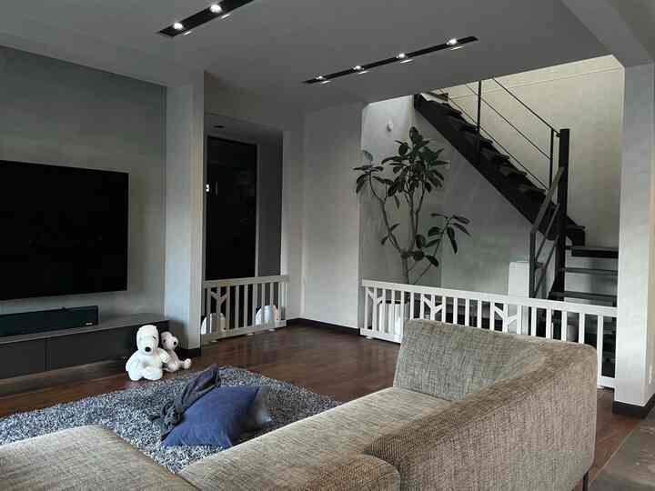 グレーの色調のリビング、ソファとテレビ壁面、赤ちゃん用安全フェンスが配置された実用的で安全な空間