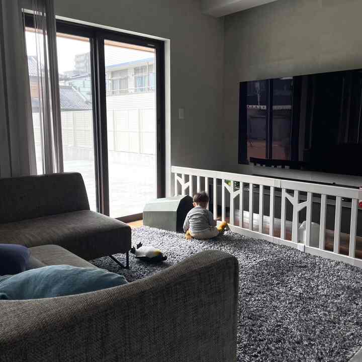 グレーとナチュラルトーンのリビング、子供と安全フェンス、スツールが配置された快適な遊び空間