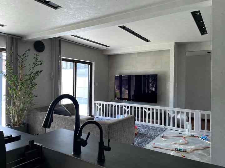 グレー調のモダンなリビングとキッチン、ソファと安全ゲート、子供の玩具が配置された開放的な空間