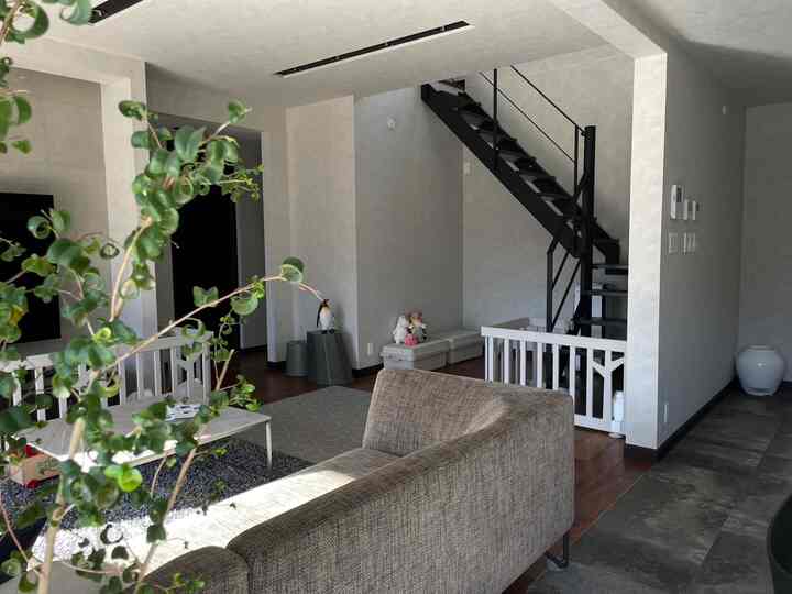 ブラウンのソファと黒い階段が配置されたモダンでナチュラルな雰囲気のリビング、子供用フェンスとおもちゃ収納を備える空間