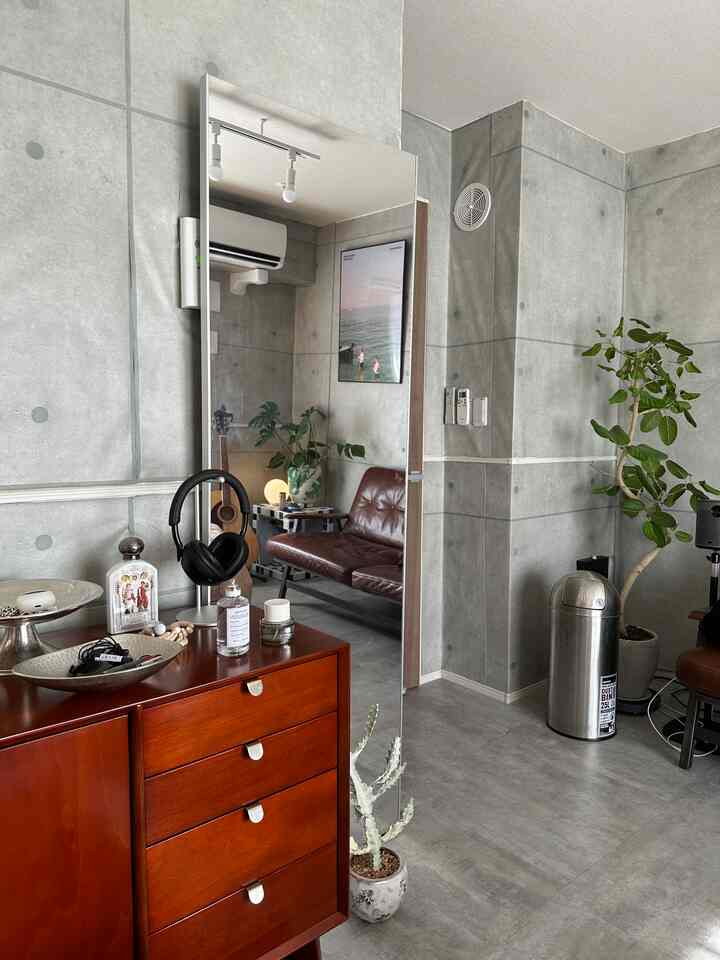 グレー調のインダストリアルスタイルのリビング、キャビネットと大きな鏡、植物が配置されたモダンなインテリア