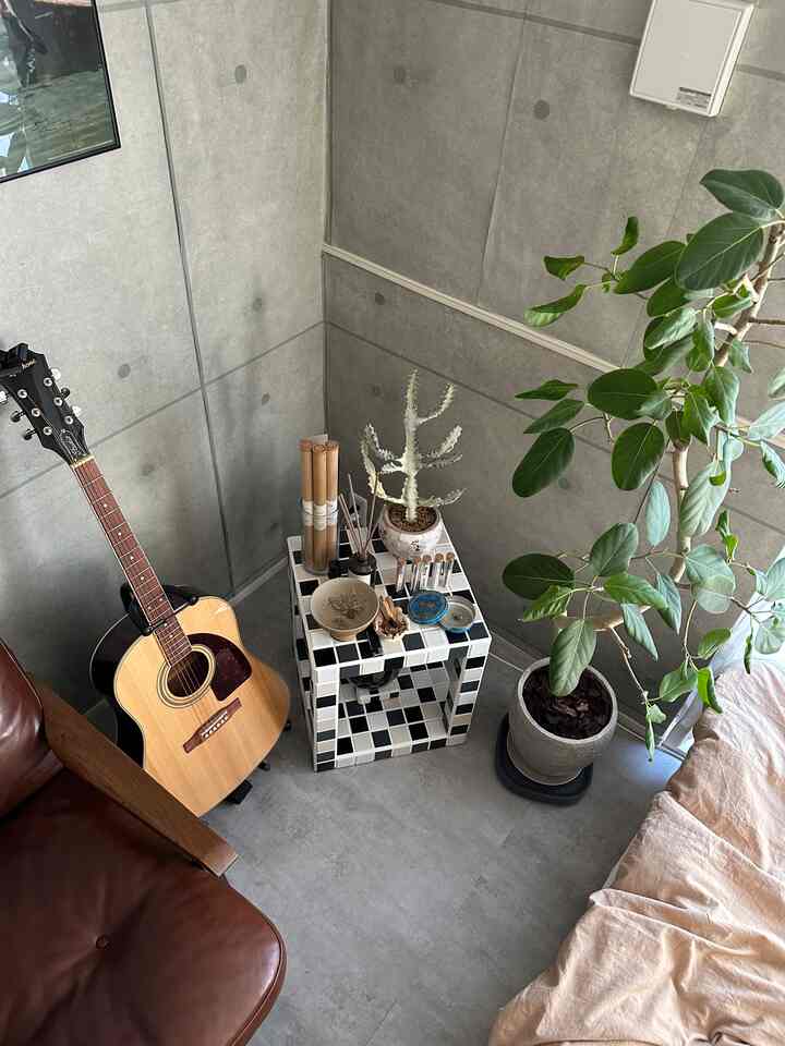 グレーのコンクリート壁とチェック柄タイルのテーブル、ブラウンレザーソファとギター、植物が置かれた自然でミッドセンチュリーモダンなコーナースペース