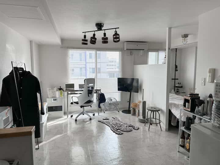 白とグレーのトーンのワンルーム、整ったレイアウトと開放感のあるホームオフィスとリビング空間