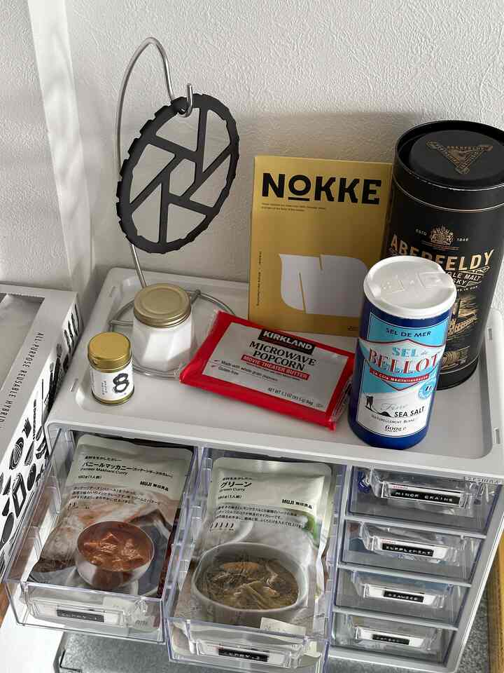 白色のキッチンスペース、透明なキャビネットに調味料やレトルト食品が整理されているミニマルな収納が印象的なインテリア