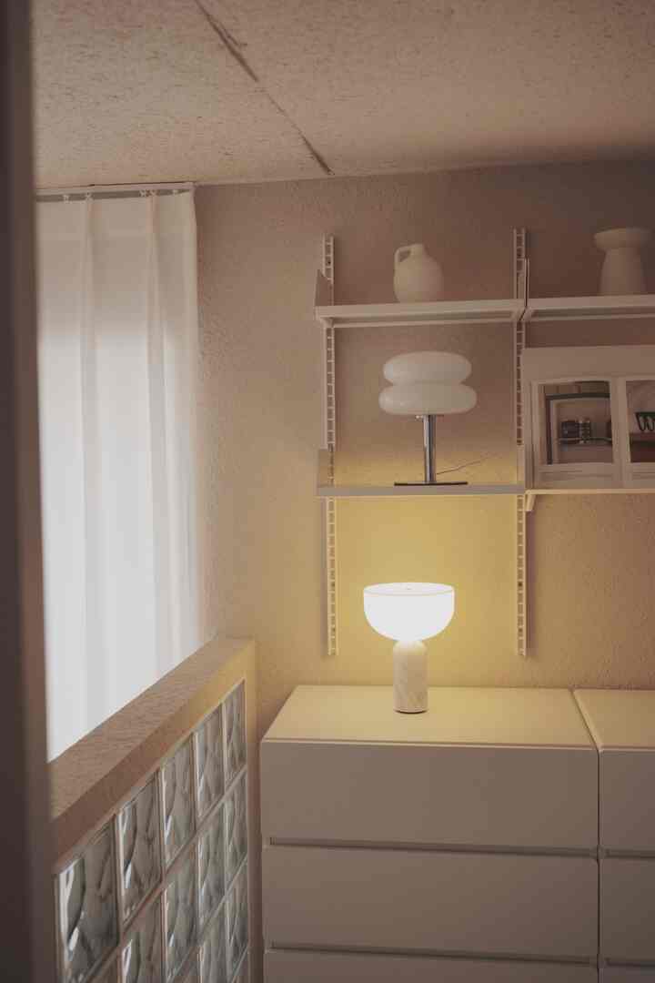 ベージュ色の壁と白い収納キャビネット、テーブルランプと棚が配置された雰囲気のある空間