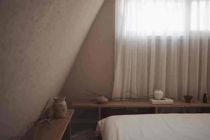 ナチュラルなベージュ色の壁と木製の棚、白いベッドが配置された落ち着いた寝室のインテリア