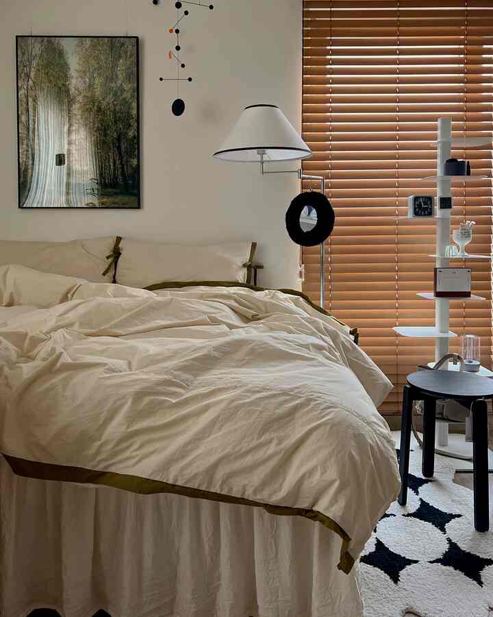 温かみのあるベージュと木目調の寝室、クリーム色のベッドとベッドスカートが整った居心地のよい空間