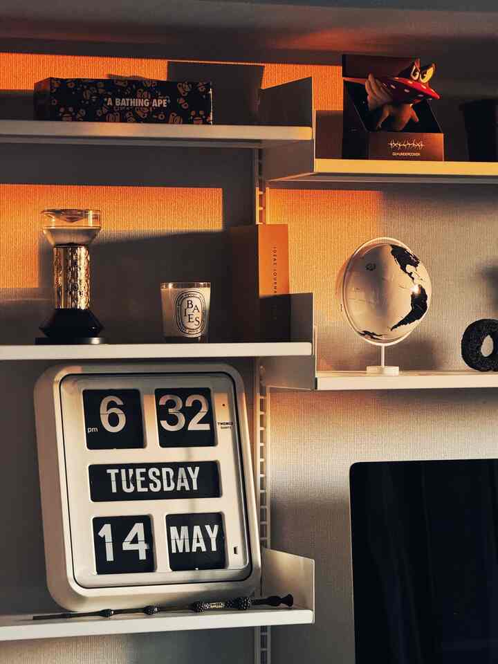 暖かい光の壁棚にフリップクロック、キャンドル、ディフューザー、地球儀などのオブジェが配置されたモダンな空間