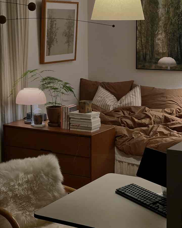 ベージュの壁と木製チェスト、ブラウンの寝具が配置されたワンルーム寝室の落ち着いた雰囲気のインテリア