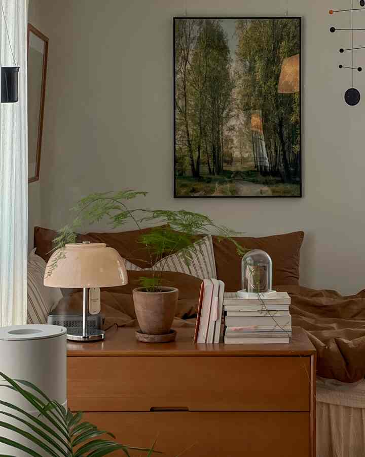 ナチュラルカラーのワンルーム寝室、木製チェストとベッド、植物、暖かいテーブルランプが配置された印象的な空間