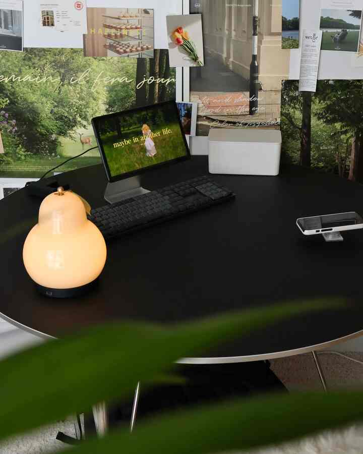 黒い円形テーブルにクリーム色のテーブルランプとキーボードが置かれたワンルームホームオフィス空間、ポスターで飾られた雰囲気のあるインテリア