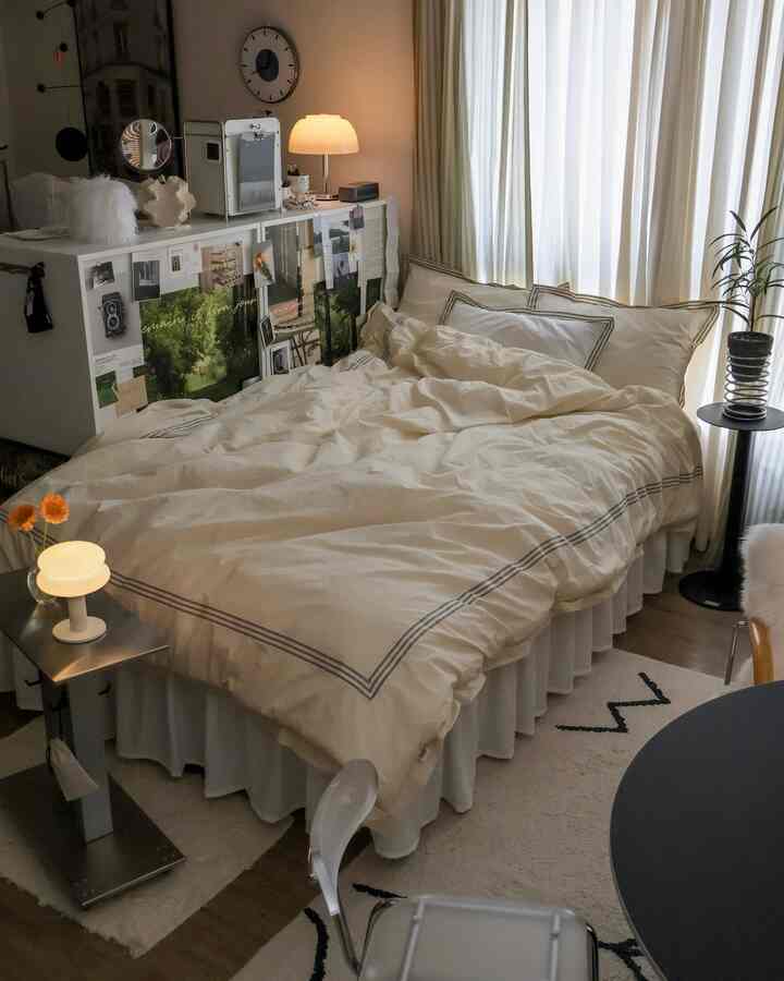 暖かいベージュとホワイトのトーンが特徴の居心地の良いワンルーム寝室、ベッドと間仕切りのワードローブ、カーテンと小さな植物が配置された空間