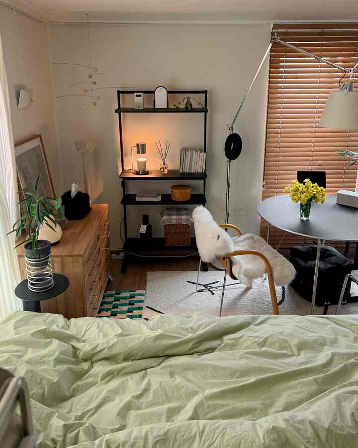 ベージュとホワイトのトーンのワンルーム寝室、木製チェストと棚、丸テーブルとアームチェアが配置された落ち着いた空間