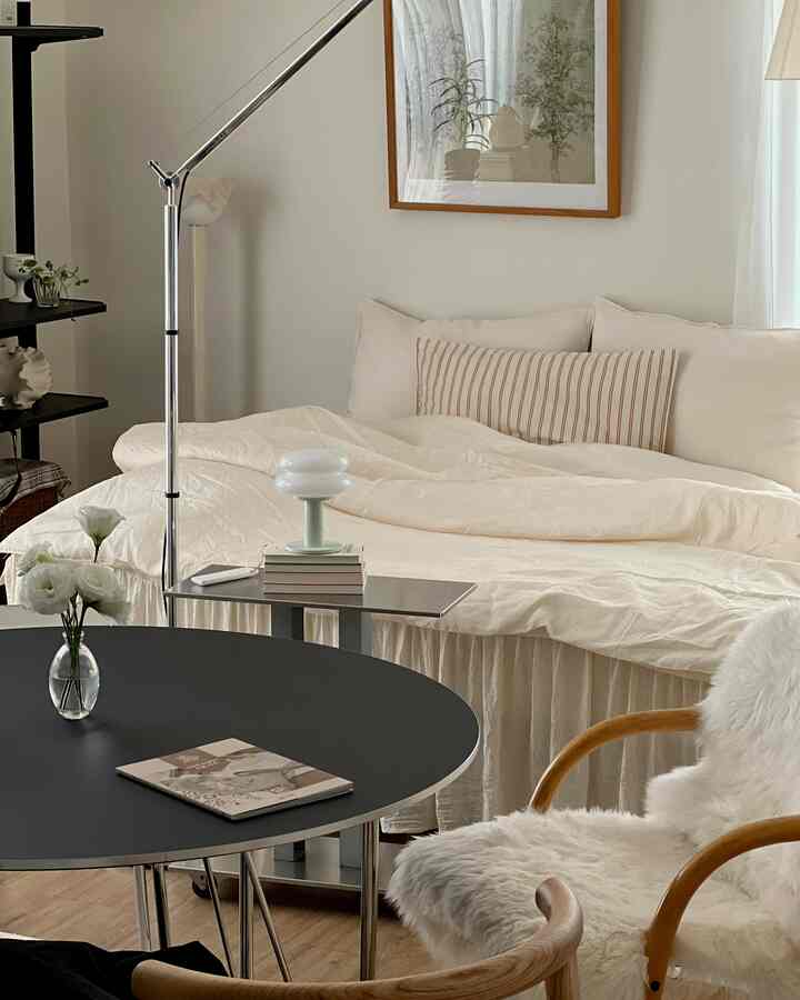 ベージュとホワイトの色調の8畳ワンルーム寝室、ベッドと木製チェア、丸い黒いテーブルが配置されたナチュラルモダンなインテリア