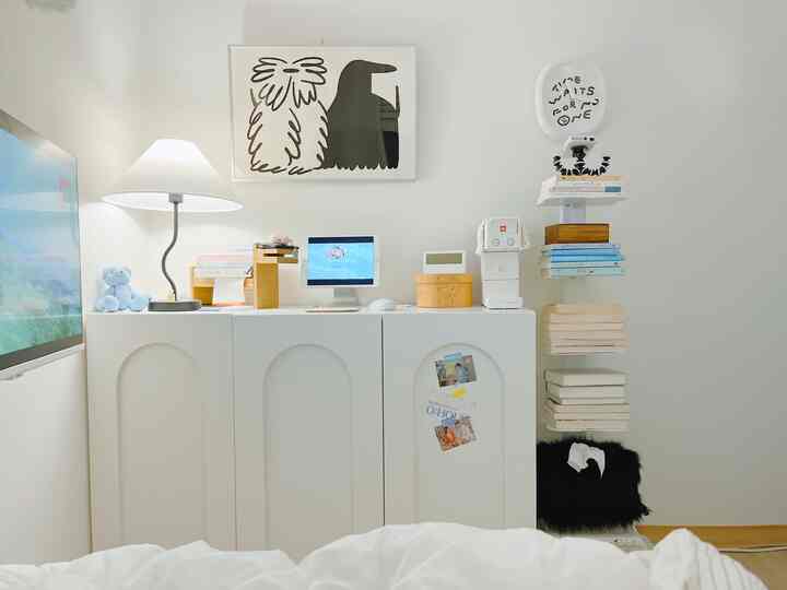 明るいホワイトトーンの寝室、白い収納キャビネット、コーヒーマシン、独特な本棚とポスターが配置された清潔感のあるインテリア