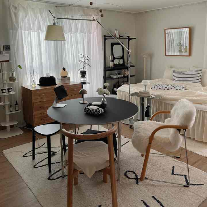 ナチュラルモダンスタイルの8坪ワンルーム、木製家具と黒い丸テーブル、白いラグが調和した居心地の良い寝室兼リビングスペース