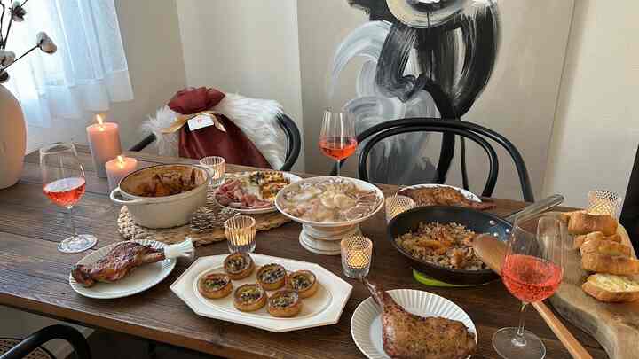 明るい白い壁とブラウンの木製ダイニングテーブルがある4人用ダイニングルーム、様々な料理とワイングラス、キャンドルが演出するホームパーティーの雰囲気のあるインテリア